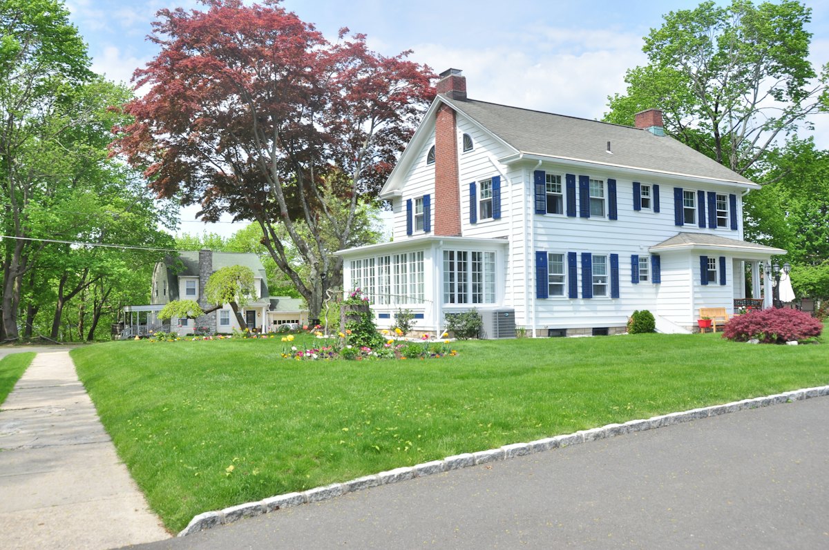 White colonial home with mature trees and a green lawn