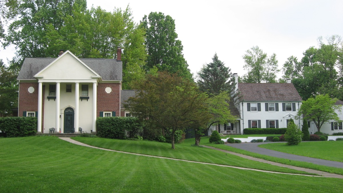 Red-brick Georgian home with a columned entry beside a white colonial